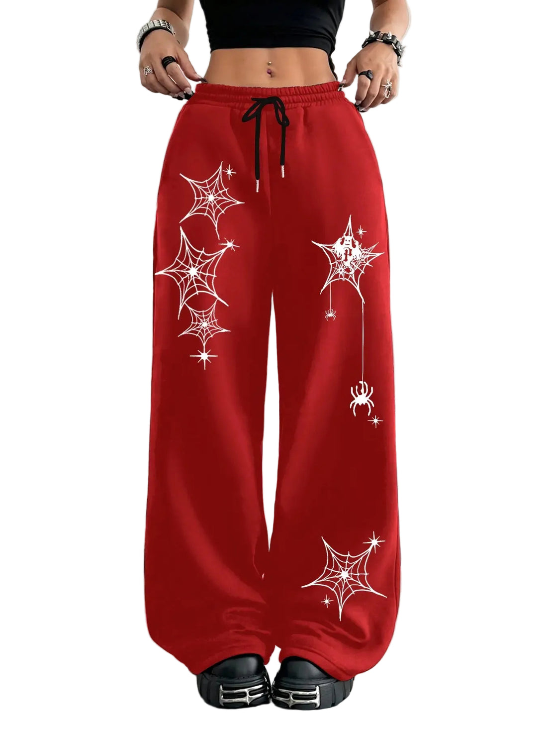 A person wearing bright red wide-leg sweatpants with white spiderweb and spider graphics, shown from the waist down in a styled indoor setting with Halloween decor. A vertical color swatch panel reading MORE COLORS appears on the left side.