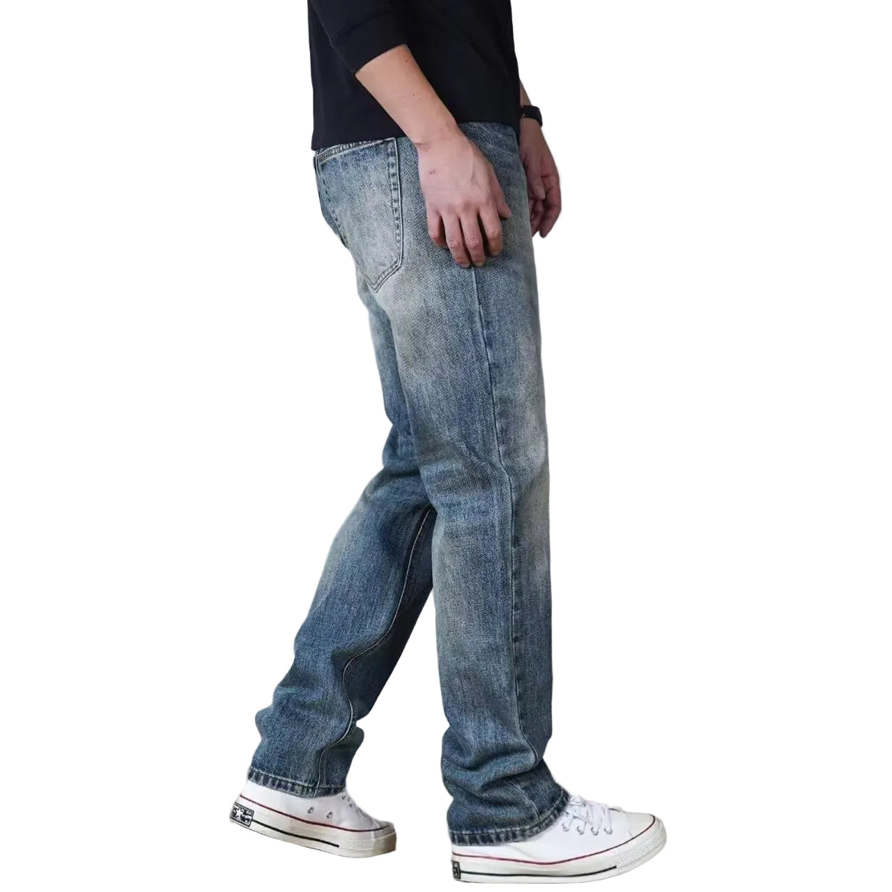 A person wearing light-wash blue denim jeans, a black t-shirt, and white low-top sneakers, shown from the waist down against a light gray studio background.