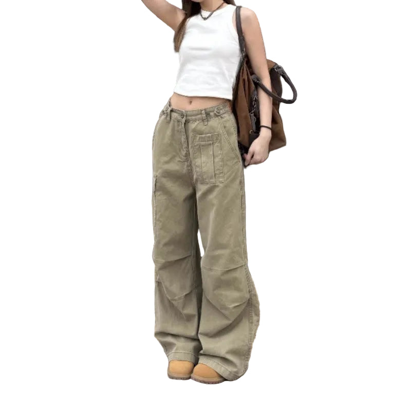 A person standing outdoors in front of a storefront wearing wide-leg olive cargo pants, a white sleeveless crop top, tan shoes, and carrying a brown shoulder bag.