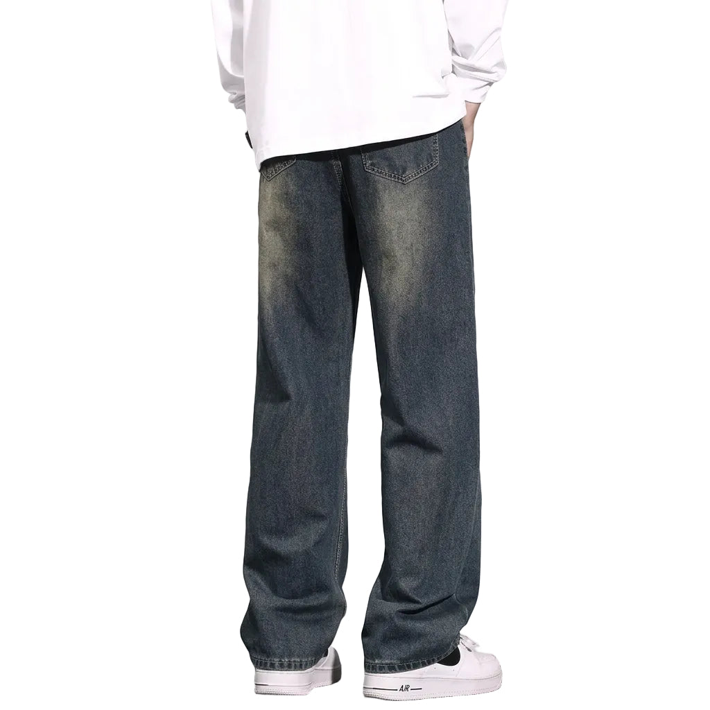 A person shown from the back wearing loose-fit dark blue denim jeans with a faded wash, a white long-sleeve shirt, and white sneakers against a plain gray studio background.