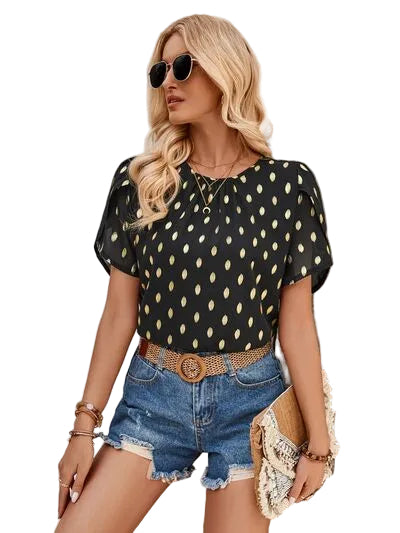 Woman wearing a black polka dot top and denim shorts, standing against a textured wall.