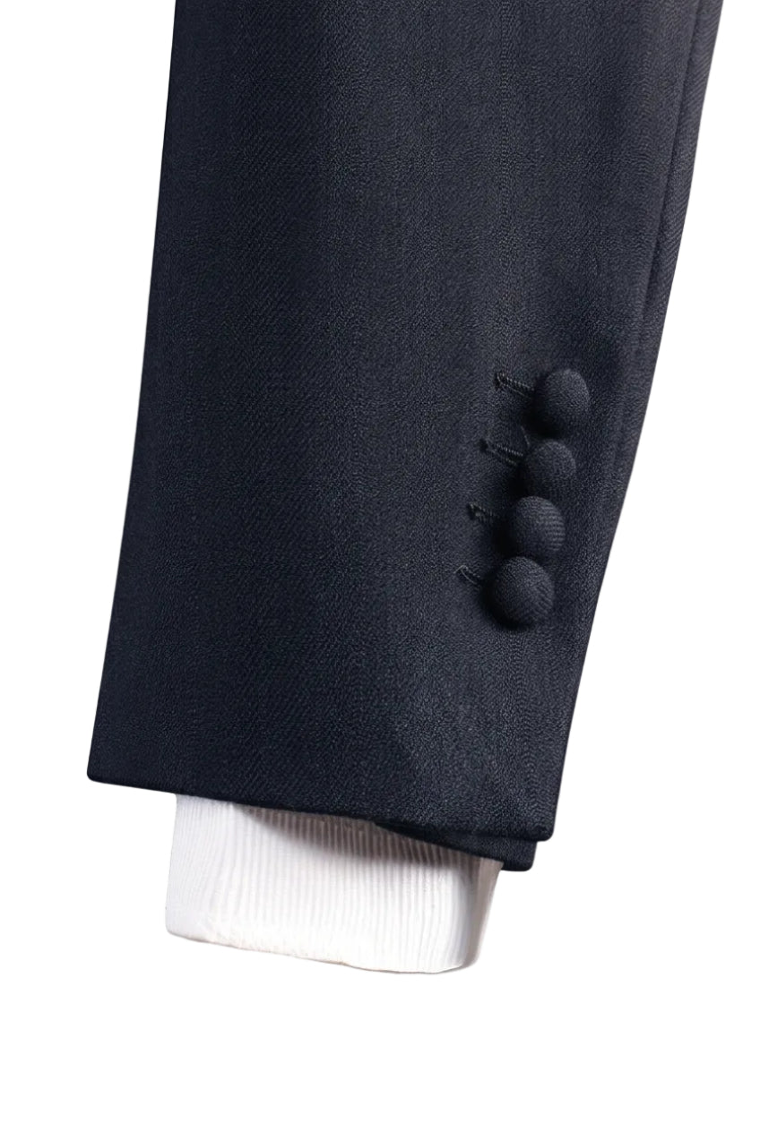 Close-up of a dark navy blazer sleeve with four decorative buttons, layered over a white dress shirt cuff, set against a solid terracotta background.