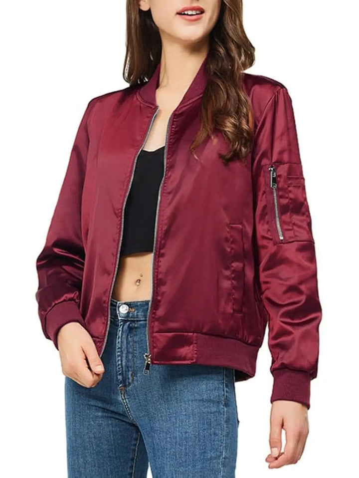 A woman wearing a shiny burgundy satin bomber jacket with a black crop top and blue jeans, shown from the chest down against a plain white background.