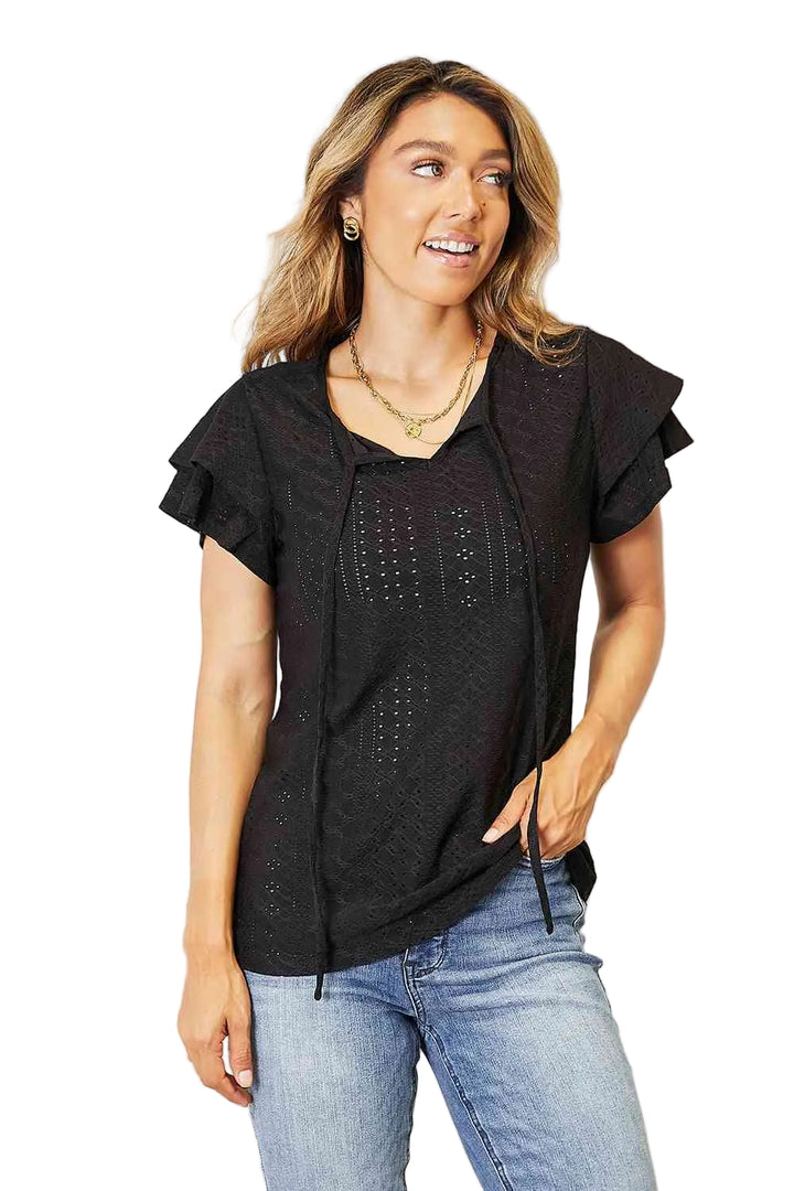 Woman wearing a black top with ruffled sleeves and blue jeans against a white background