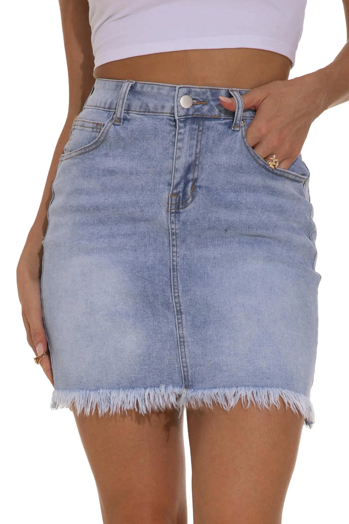 A light blue denim mini skirt with a raw, frayed hem, shown on a model wearing a white crop top against a white background.