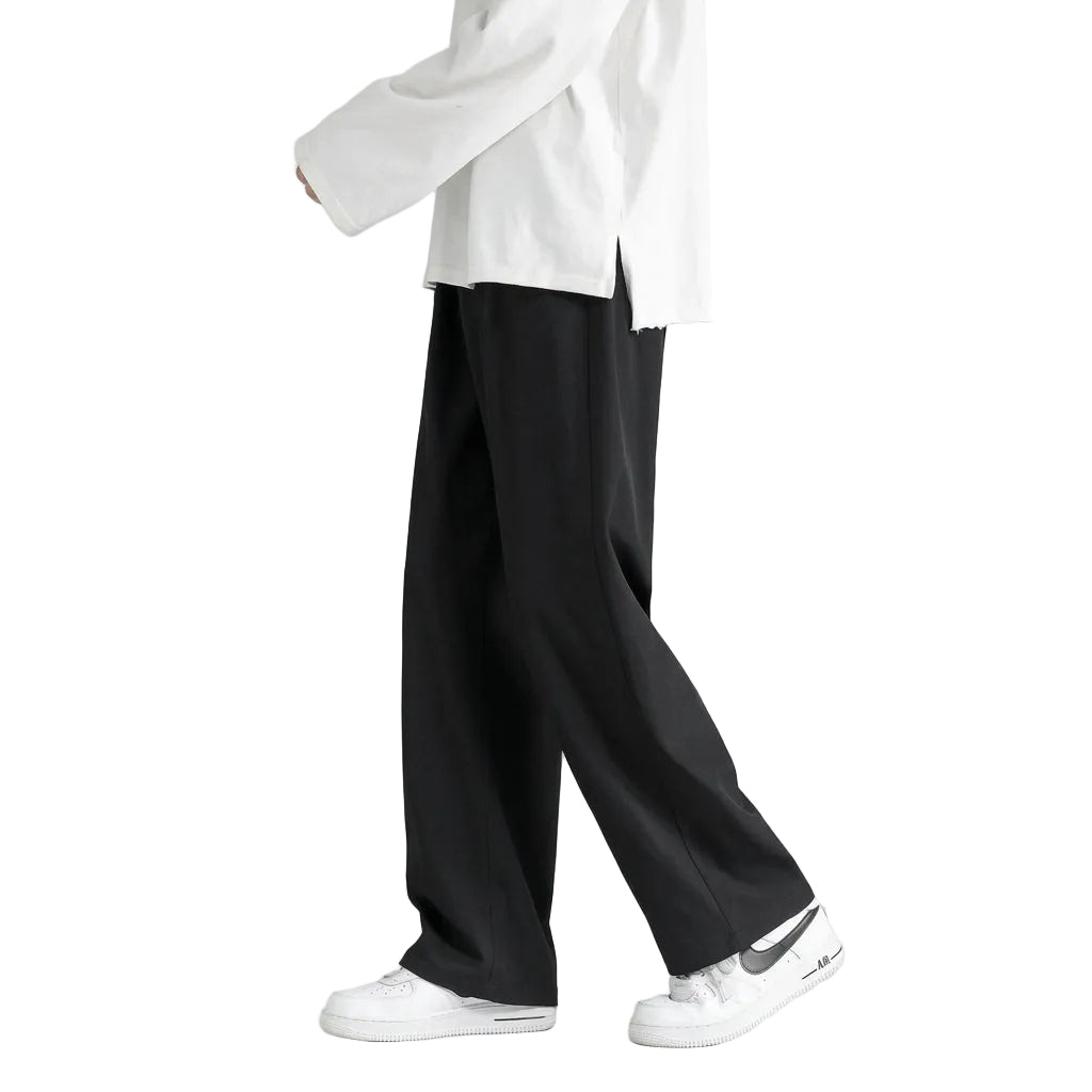 A person wearing loose black wide-leg pants, a white top, and white sneakers, shown from the waist down against a plain olive-gray studio background.