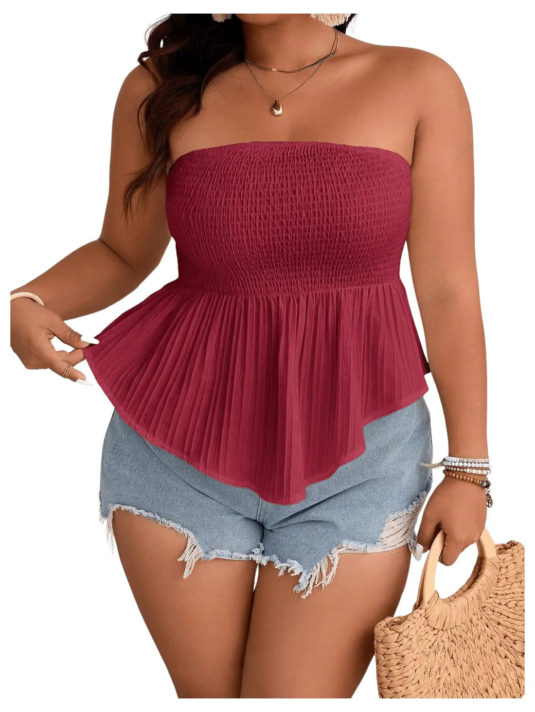 Woman wearing a red strapless top and denim shorts, holding a straw bag on a white background