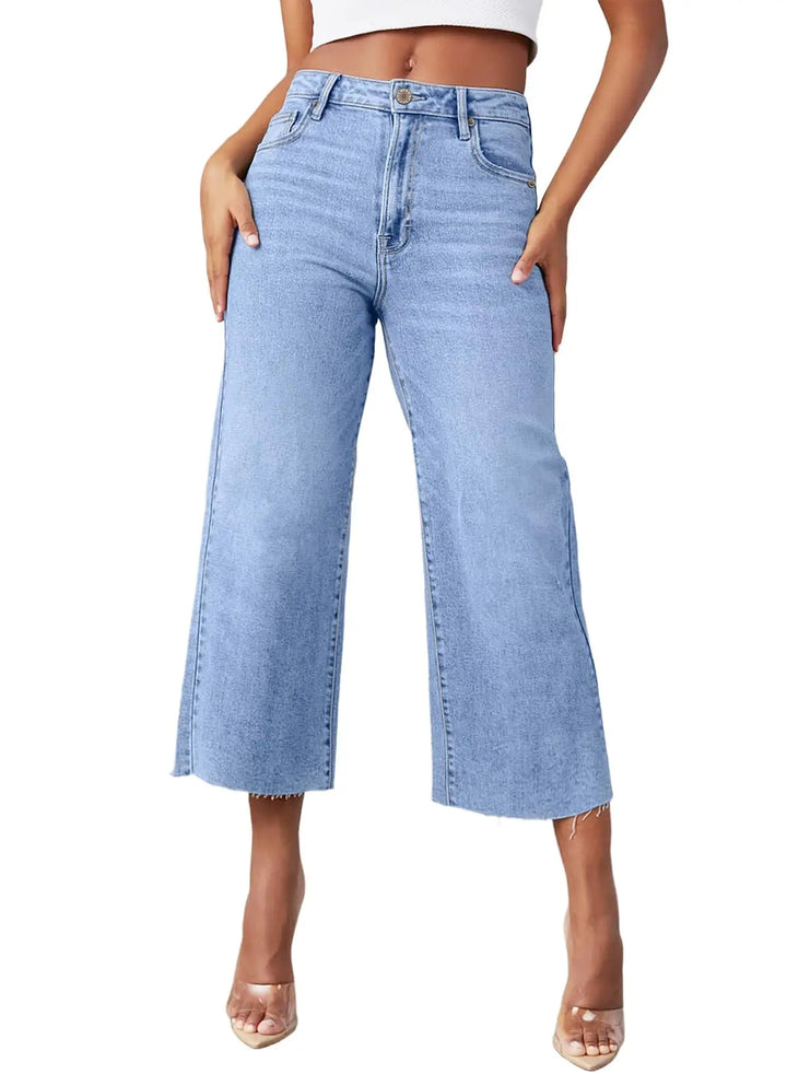 A model wearing light blue high-waisted cropped flare jeans with a raw hem, paired with a white crop top and clear high-heeled sandals, shown against a plain white background.