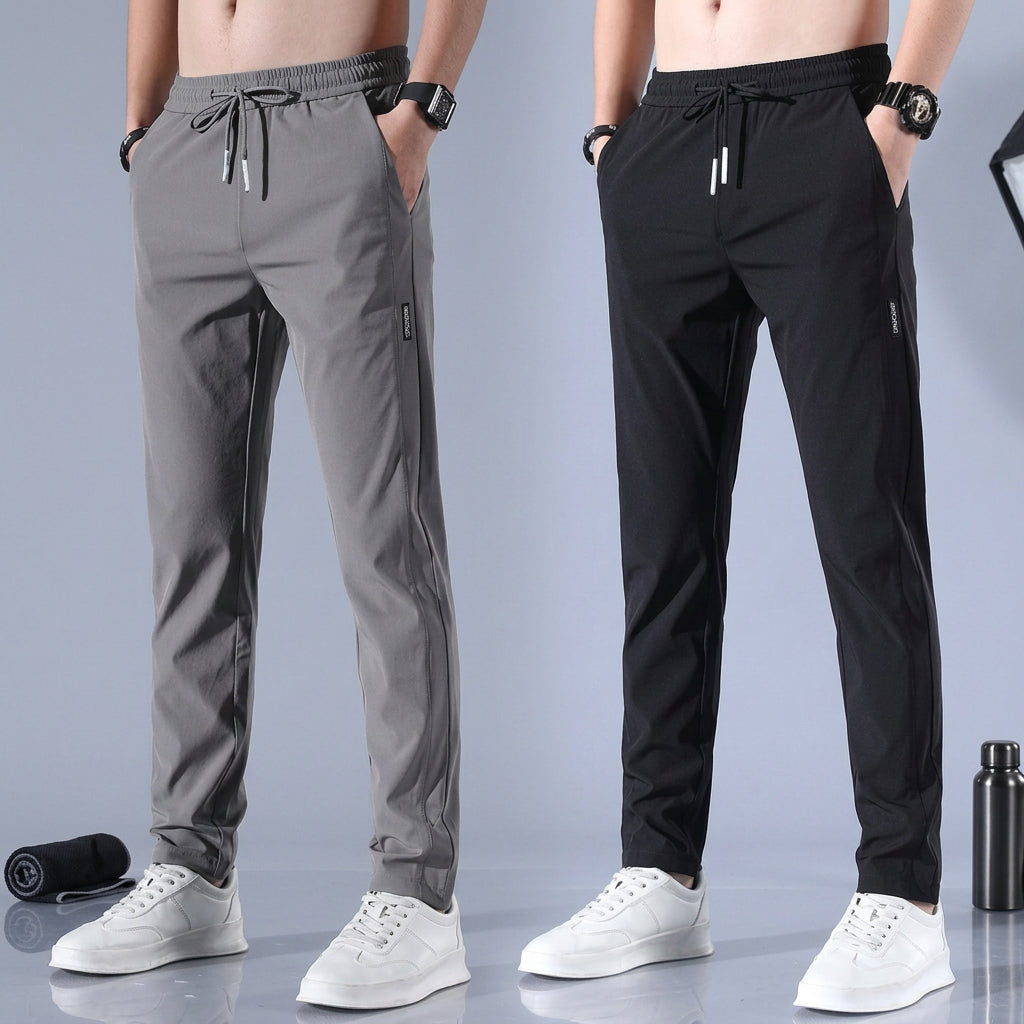 Two pairs of men's athletic jogger pants shown on cropped male models: one pair is gray and the other is black. Both pants have drawstring waistbands, side pockets, and are paired with white sneakers against a clean studio backdrop.