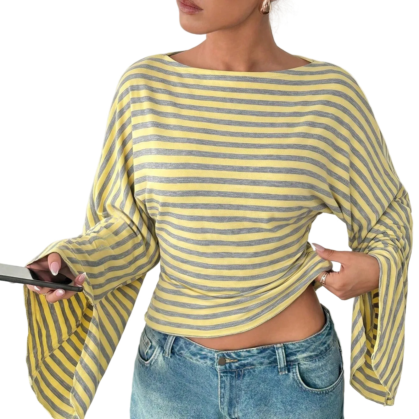 A woman wearing a yellow and gray striped long-sleeve top with wide bell sleeves, paired with blue jeans, holding a black smartphone.