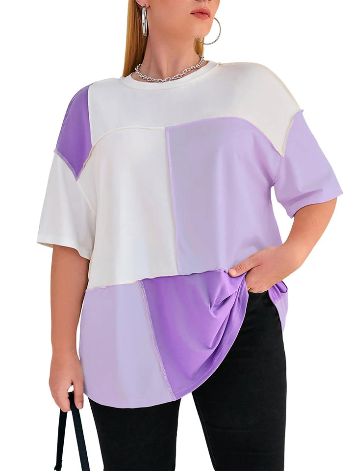 A woman wearing a loose, short-sleeve colorblock top with white and lavender panels, paired with black pants against a plain white background.