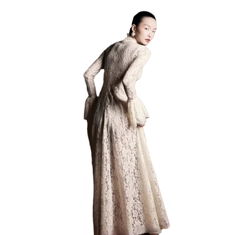 A woman wearing a long-sleeved cream lace dress, photographed from behind against a dark, textured brown studio background.