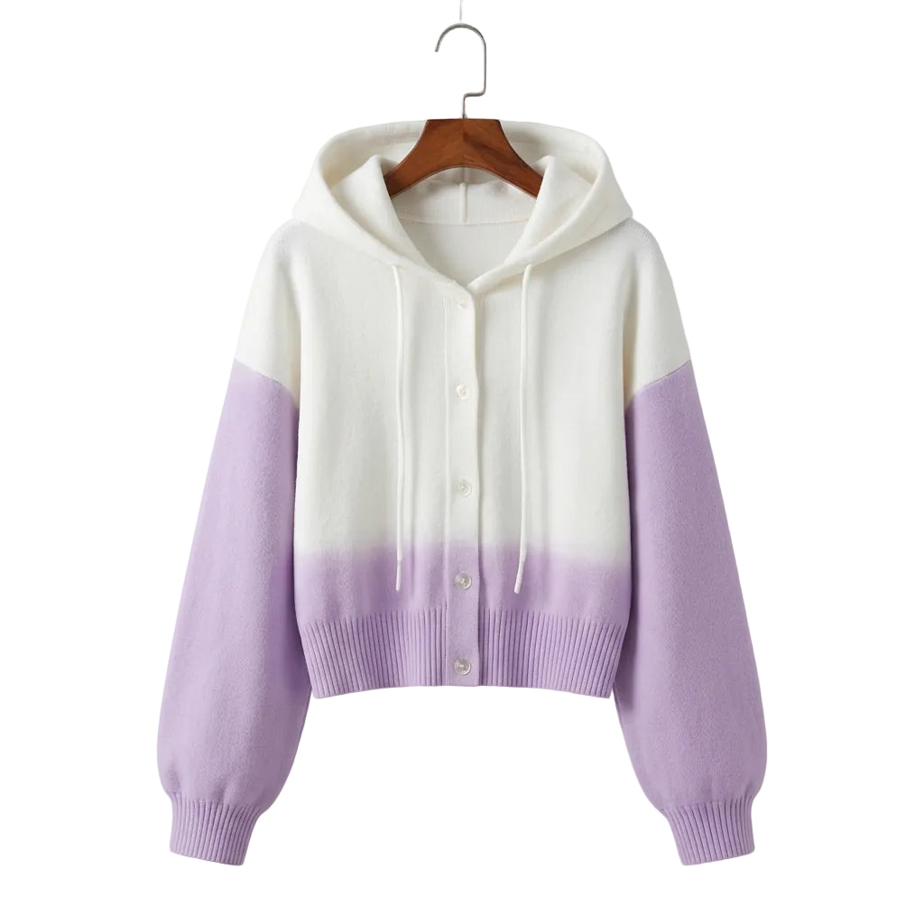 A pastel-colored hooded cardigan sweater with a white upper body and lavender-purple lower body and sleeves, styled on a light-colored table with a keyboard, pearl necklace, and small pink purse in the background.