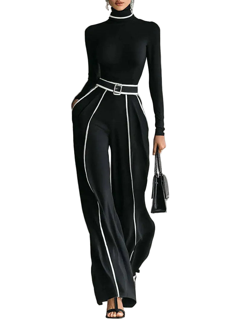 A model wears a black long-sleeve mock-neck top and matching high-waisted wide-leg trousers with contrasting white piping and a white belt. She is holding a black handbag and wearing black strappy heels against a gray studio background.