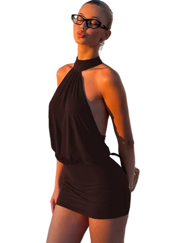 Woman in a black halter neck dress standing on a beach with buildings in the background