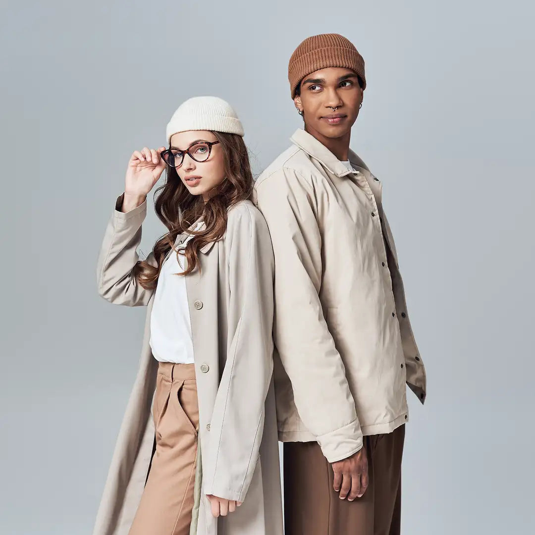 A pair of models wearing coordinated beige trench coat and matching beanie outfits.